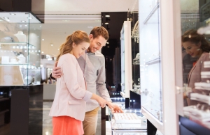 concepto de venta, consumismo, compras y personas - pareja feliz eligiendo el anillo de compromiso en la joyería en el centro comercial